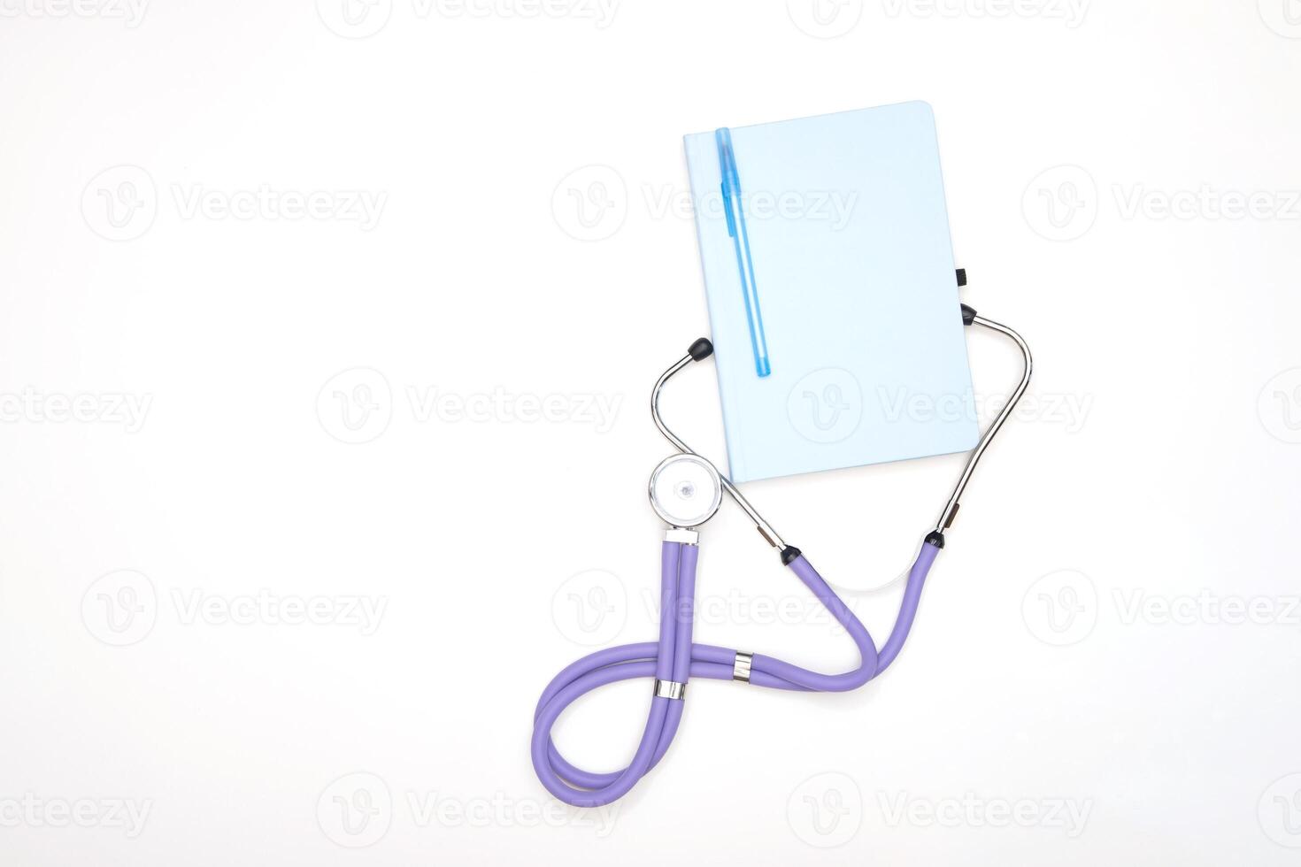 A lilac phonendoscope lies on a table with a notepad and a pen, view from above photo