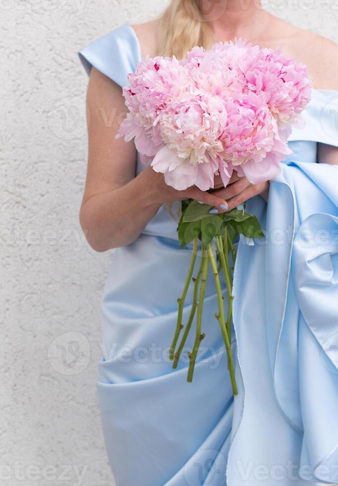 novia en un azul Boda vestir con un ramo de flores de rosado peonias, pastel paraíso foto