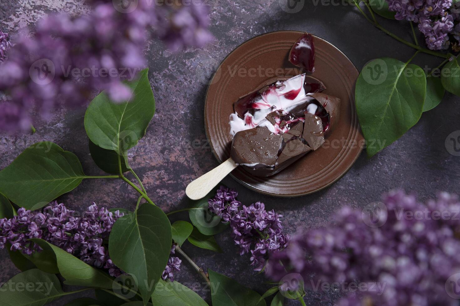 melted raspberry ice cream in chocolate on a wooden stick on a dark table photo