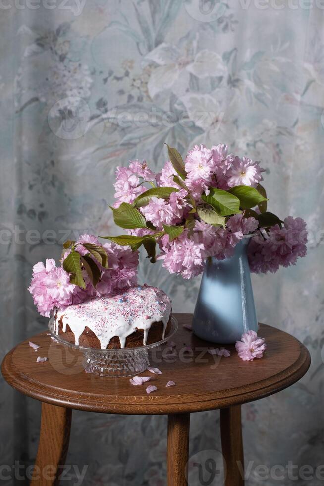 Easter cake and painted eggs and a bouquet of pink sakura flowers on a table photo