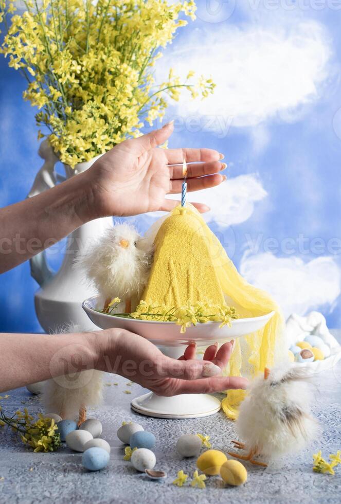 a woman lights a candle on a traditional yellow Slavic Easter curd cake photo