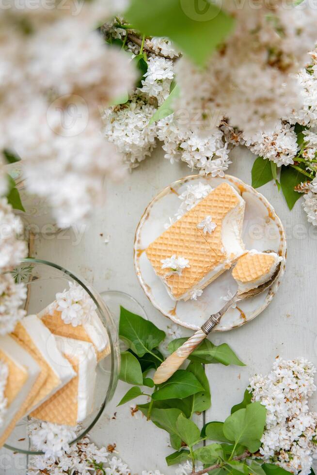 mordido gofre hielo crema en cuenco y en un platillo, primavera todavía vida con ramo de flores de blanco lilas,antiguo porcelana conjunto foto