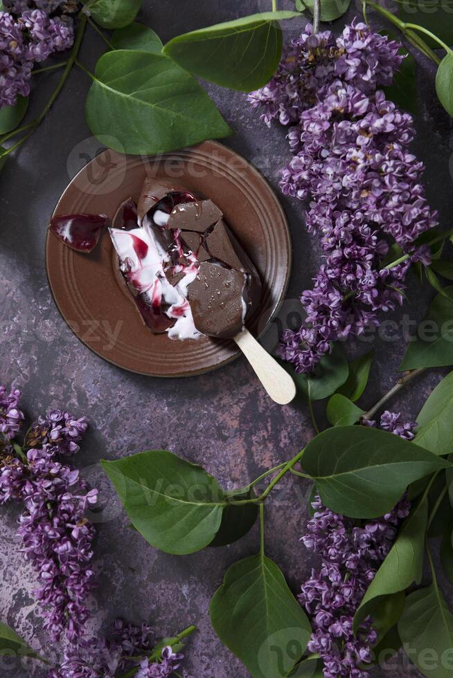 Derretido frambuesa hielo crema en chocolate en un de madera palo en un oscuro mesa foto