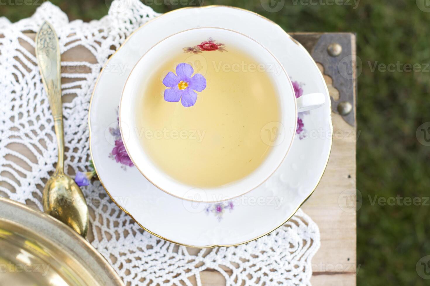 porcelain cup with tea and flower floats in tea, vintage still life, top view photo