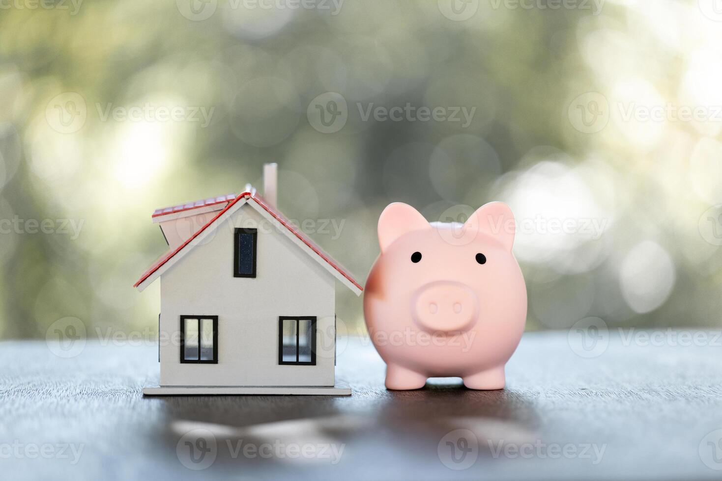 Model of house with piggy bank on table on blurred background. Money saving or investing for home loan or real estate. Investment property, Saving money for retirement concept. photo