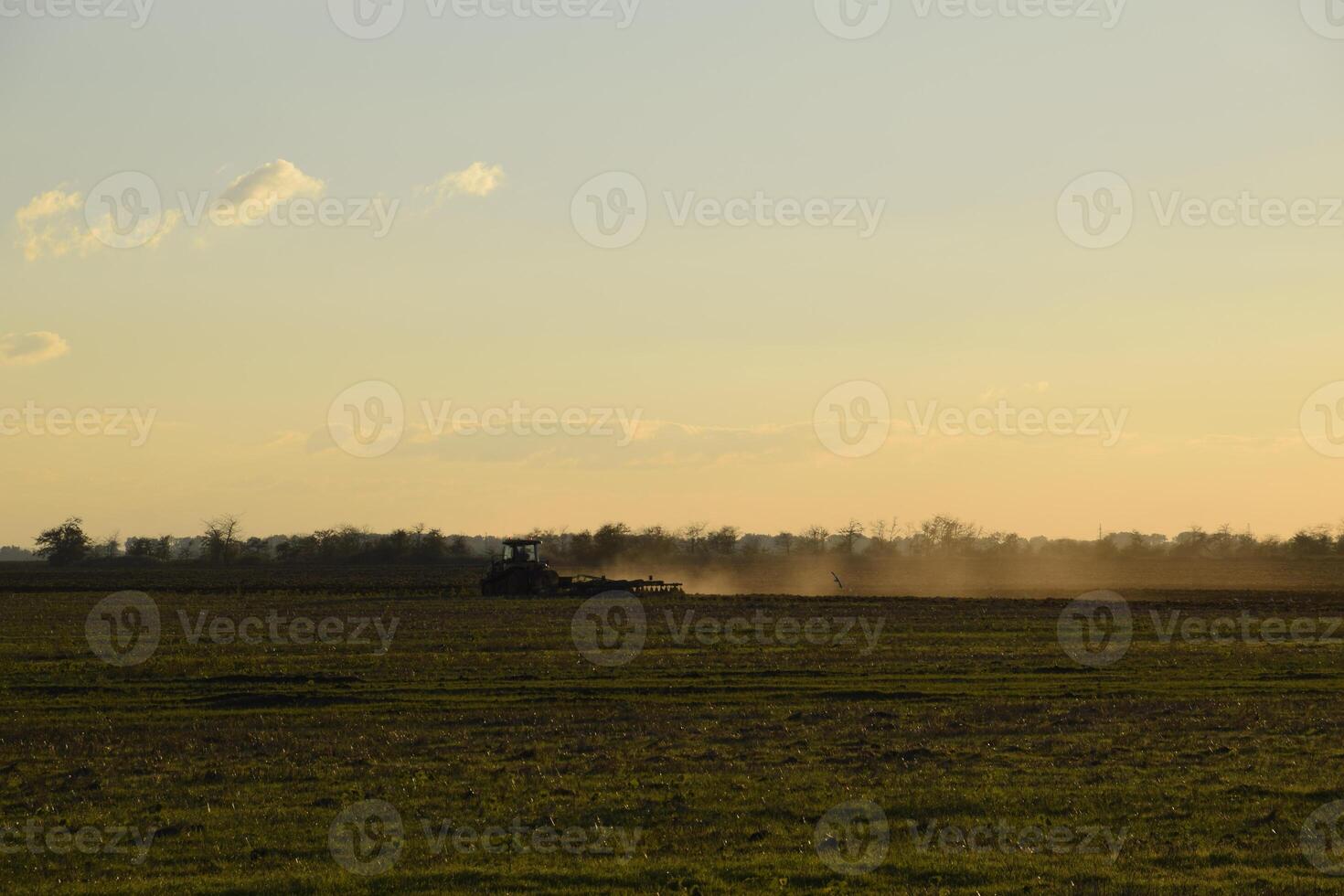 Tractor at sunset plow plow a field. Tilling the soil in the fall after harvest. The end of the season photo