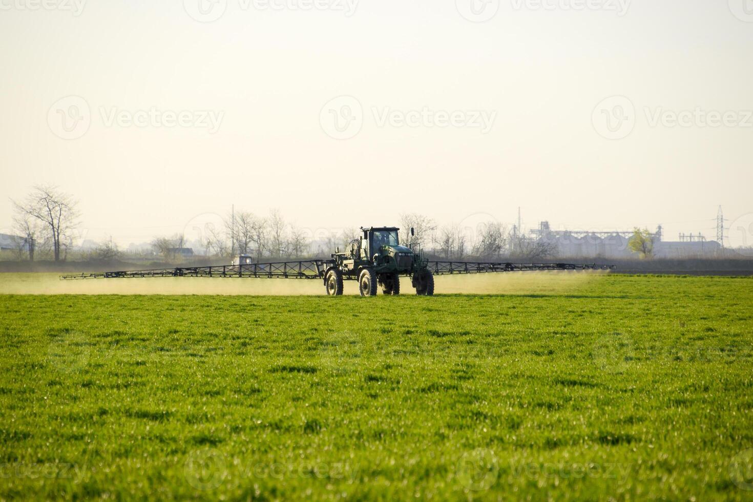Tractor on the sunset background. Tractor with high wheels is making fertilizer on young wheat. The use of finely dispersed spray chemicals photo