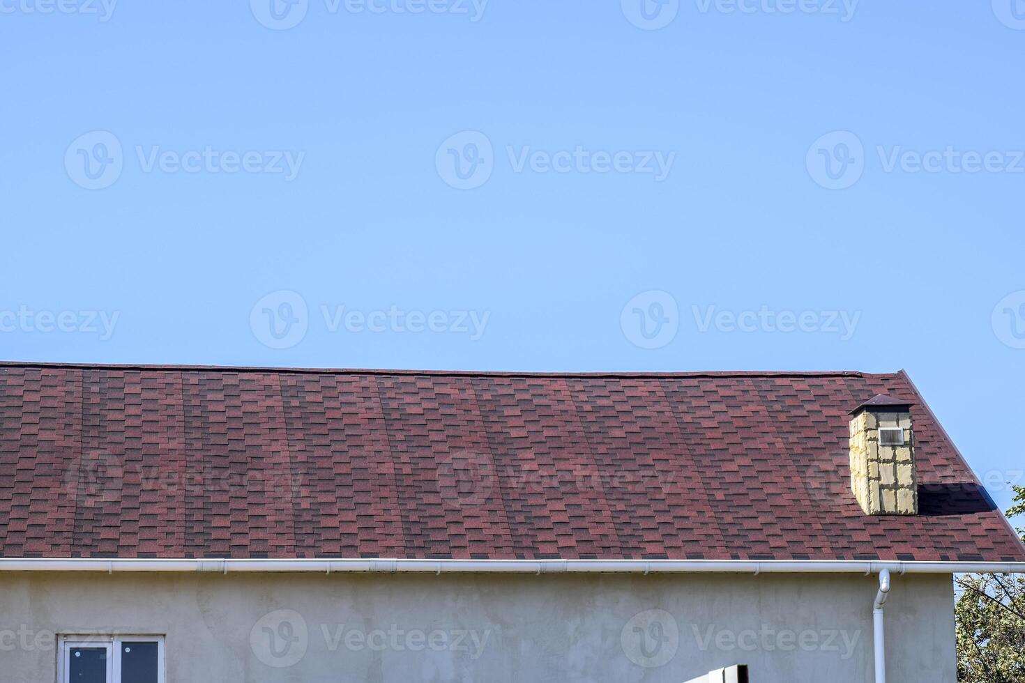 Roof from multi-colored bituminous shingles. Patterned bitumen shingles. Bituminous burgundy roof. photo