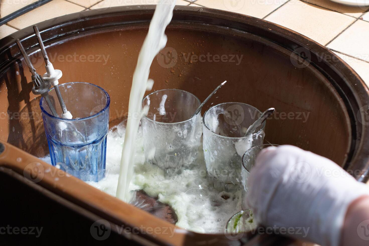 woman washing dishes in the sink with gloves with detergent photo