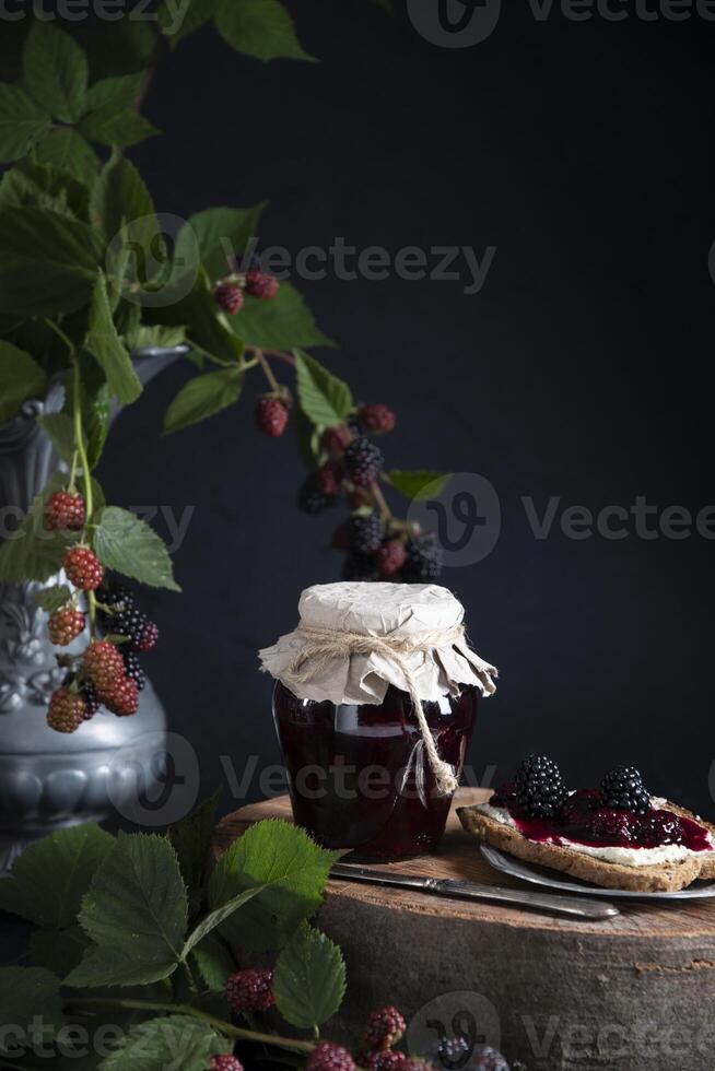 a jar of blackberry jam and bruschettas with soft cheese and berries photo