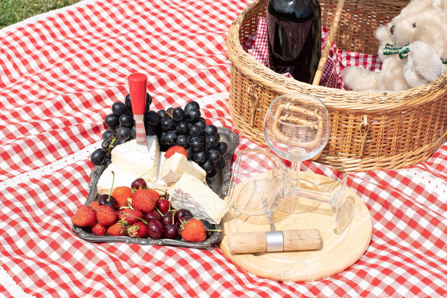 summer picnic on a green lawn with red wine, cheese and fresh berries, grapes photo