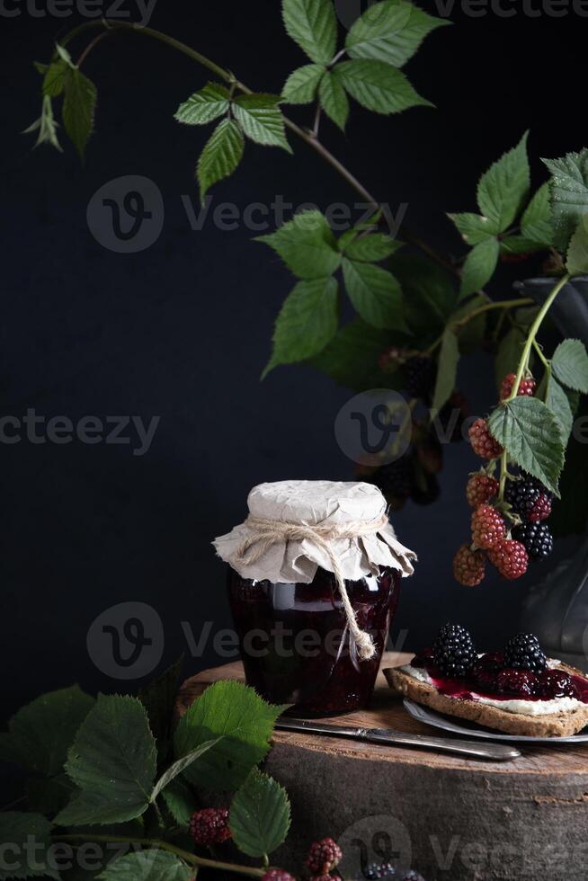 a jar of blackberry jam and bruschettas with soft cheese and berries photo