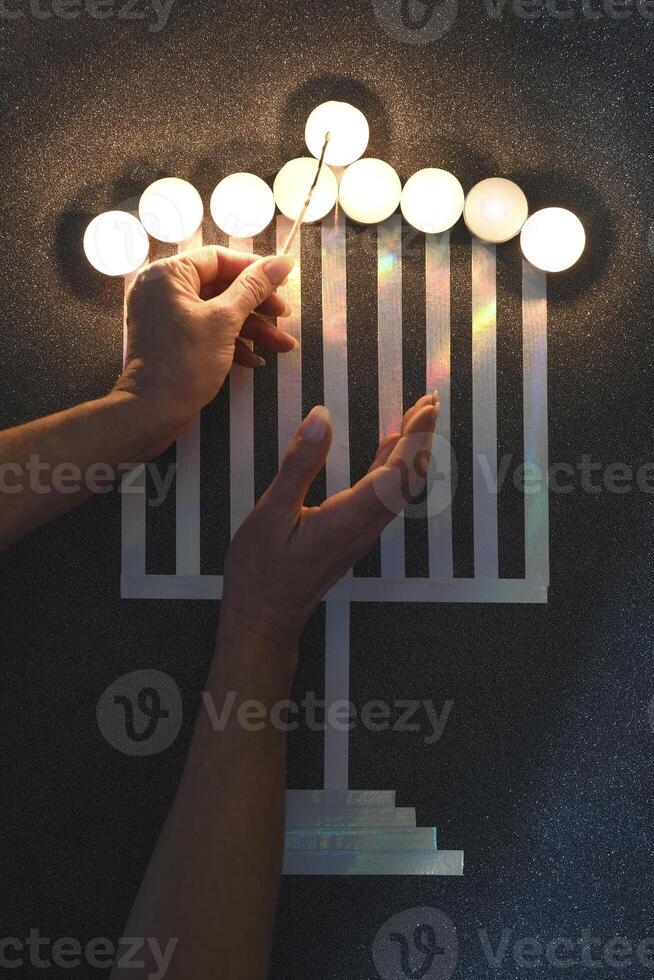 A woman's hand lights the candles of a stylized candlestick on the table, with the Jewish holiday Hanukkah photo
