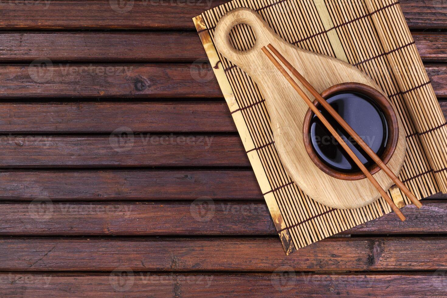 Background for sushi. Bamboo mat, soy sauce, chopsticks on wooden table. Top view and copy space photo