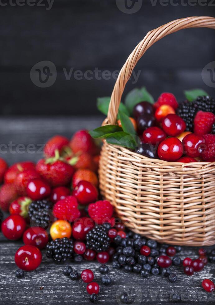 Berries mix in basket on dark wooden background photo