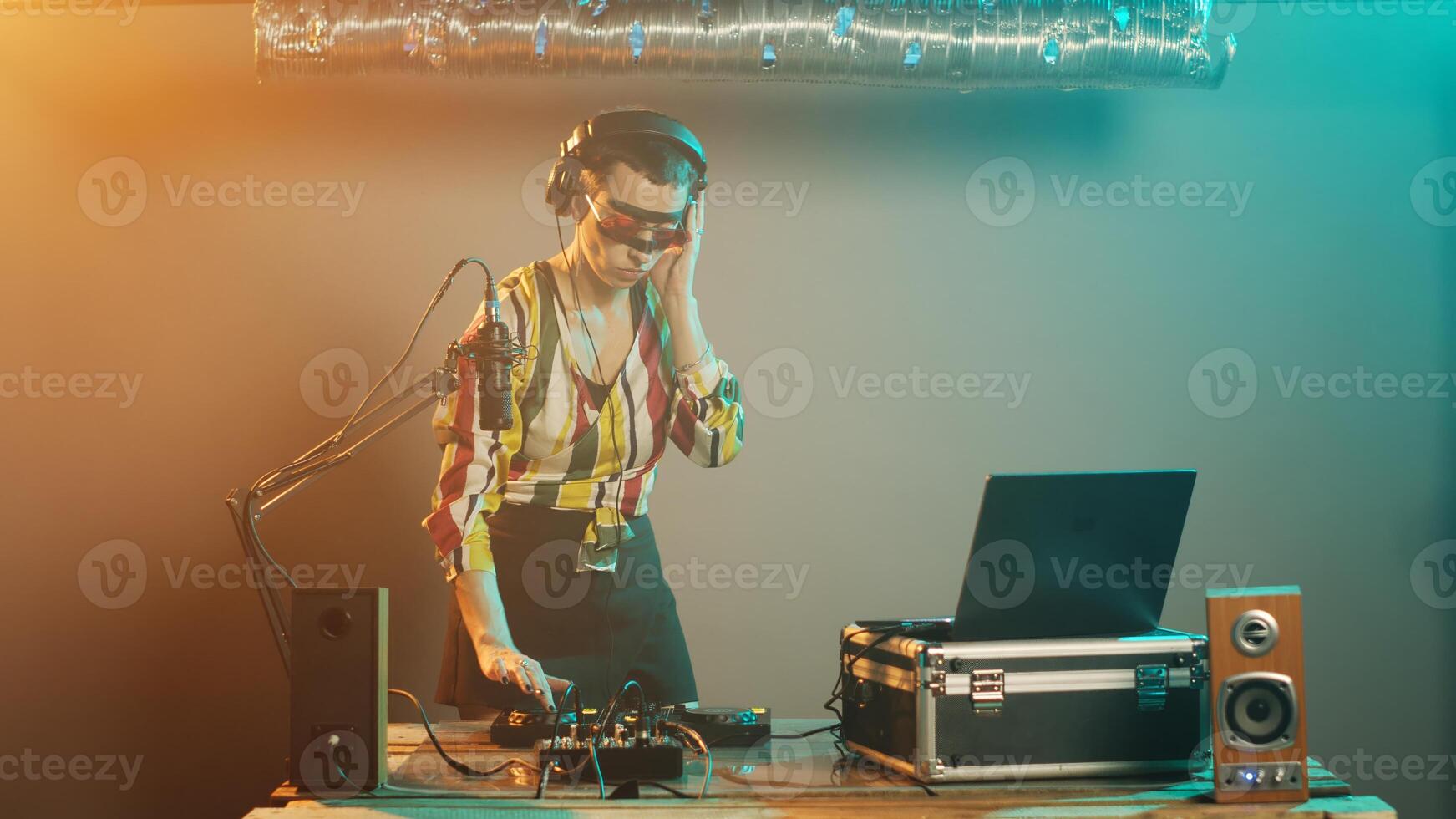 Female disc jockey producing techno music at mixer, having crazy makeup and playing with stereo instruments. Musician DJ mixing sounds at turntables to perform musical disco show. Tripod shot. photo