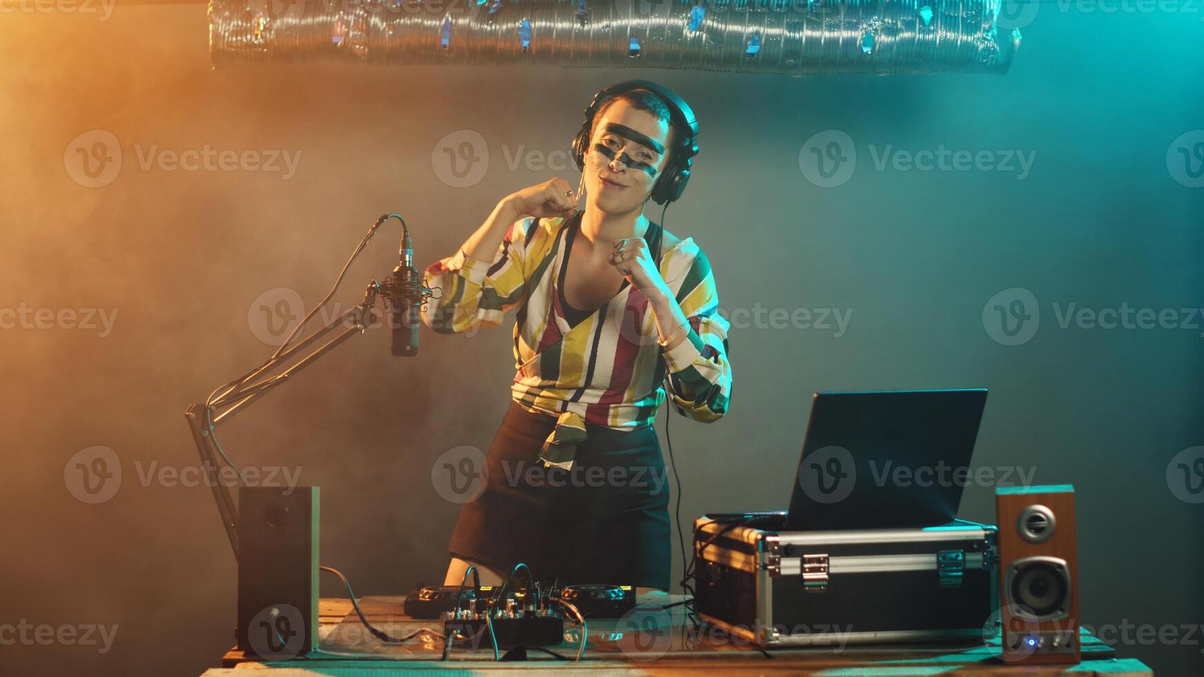 Strong performer with clenched fists creating techno remix with turntables discs and buttons, showing talent and strength on stage at disco club. Young woman artist preparing to fight. Tripod shot. photo