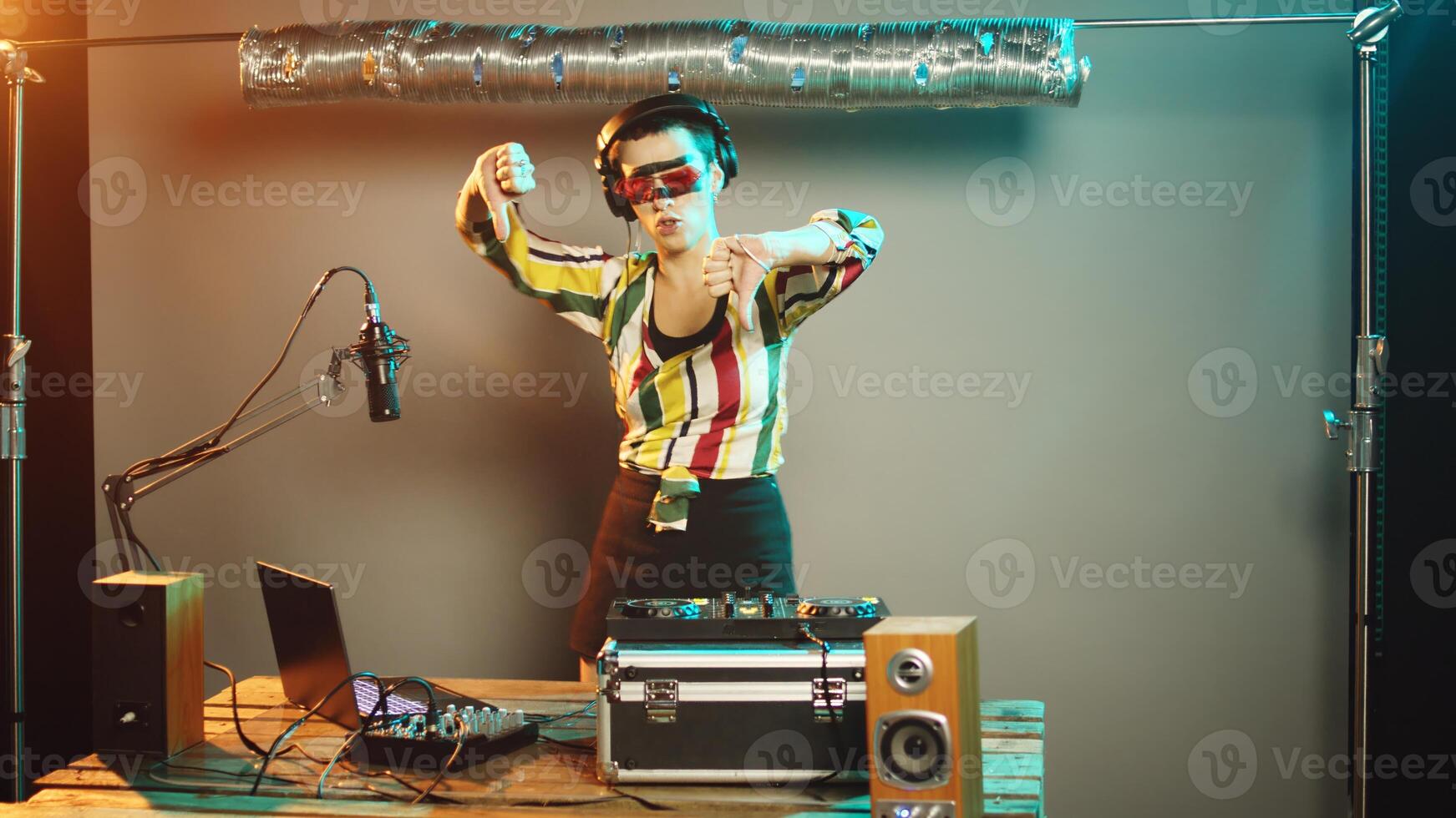 Musician artist does thumbs down on stage at nightclub, trying to use stereo turntables for techno music. Young performer mixing modern tunes as disc jockey, showing disapproval. Handheld shot. photo