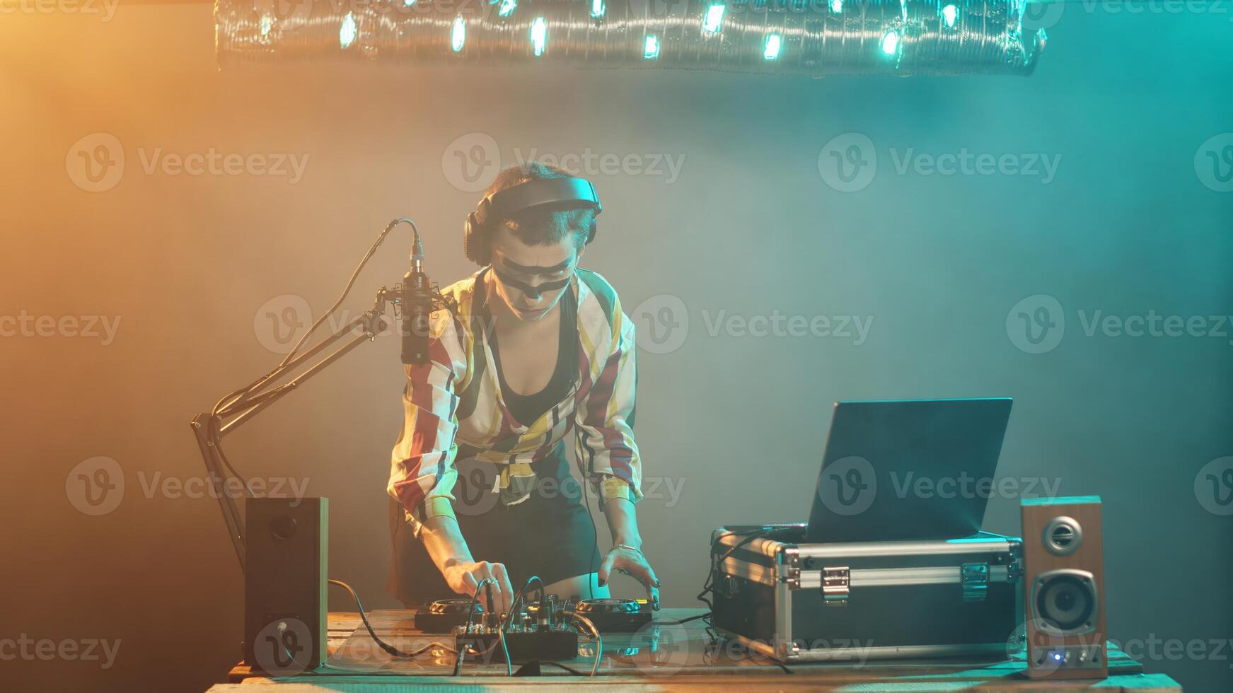 Young artist mixing with turntables on stage, preparing to mash techno and disco music to have fun at nightclub party. DJ performer with crazy makeup using mixer on table. Tripod shot. photo