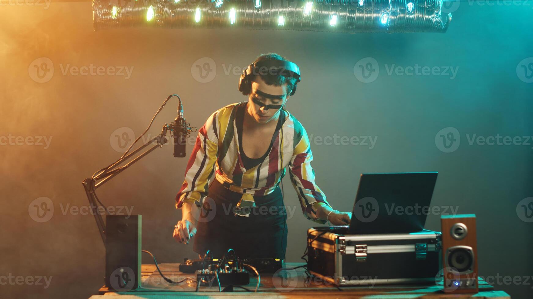 Young musician acting cool looking at mixer, focused on bass control buttons at turntables equipment over smoky background. Working with audio equipment to mix sounds. Tripod shot. photo