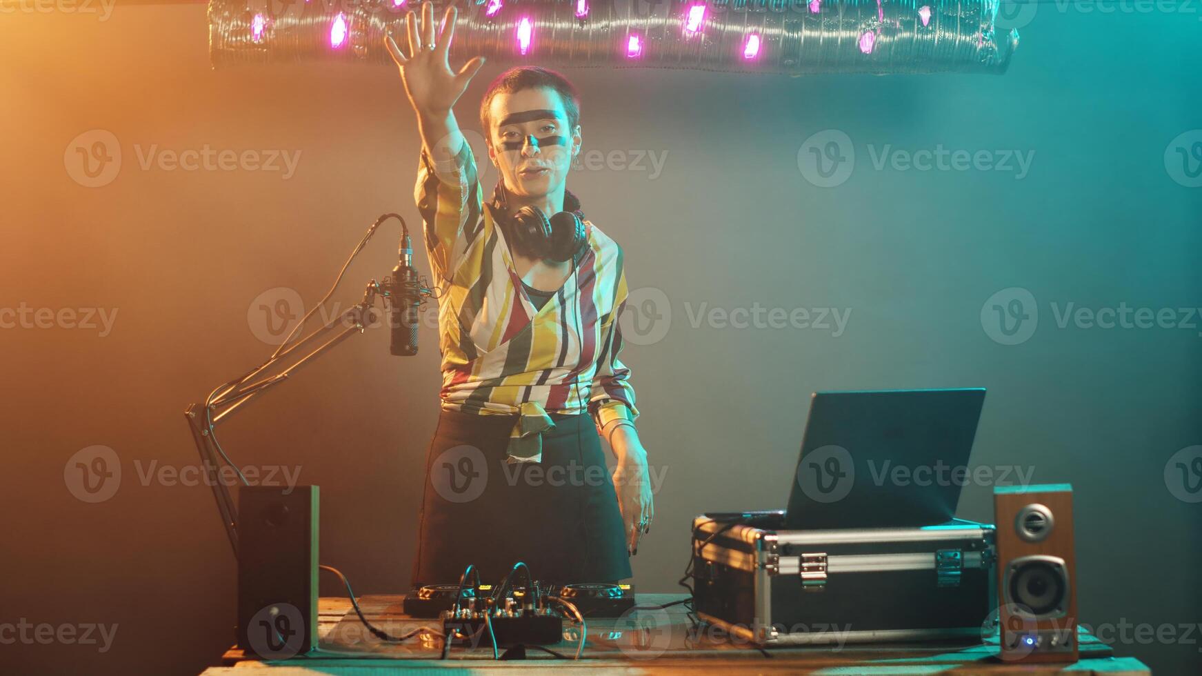 Cool musician presenting stop sign with palm raised, mixing modern sounds using headphones at turntables. Female DJ artist creating rejection and denial symbol at club. Tripod shot. photo