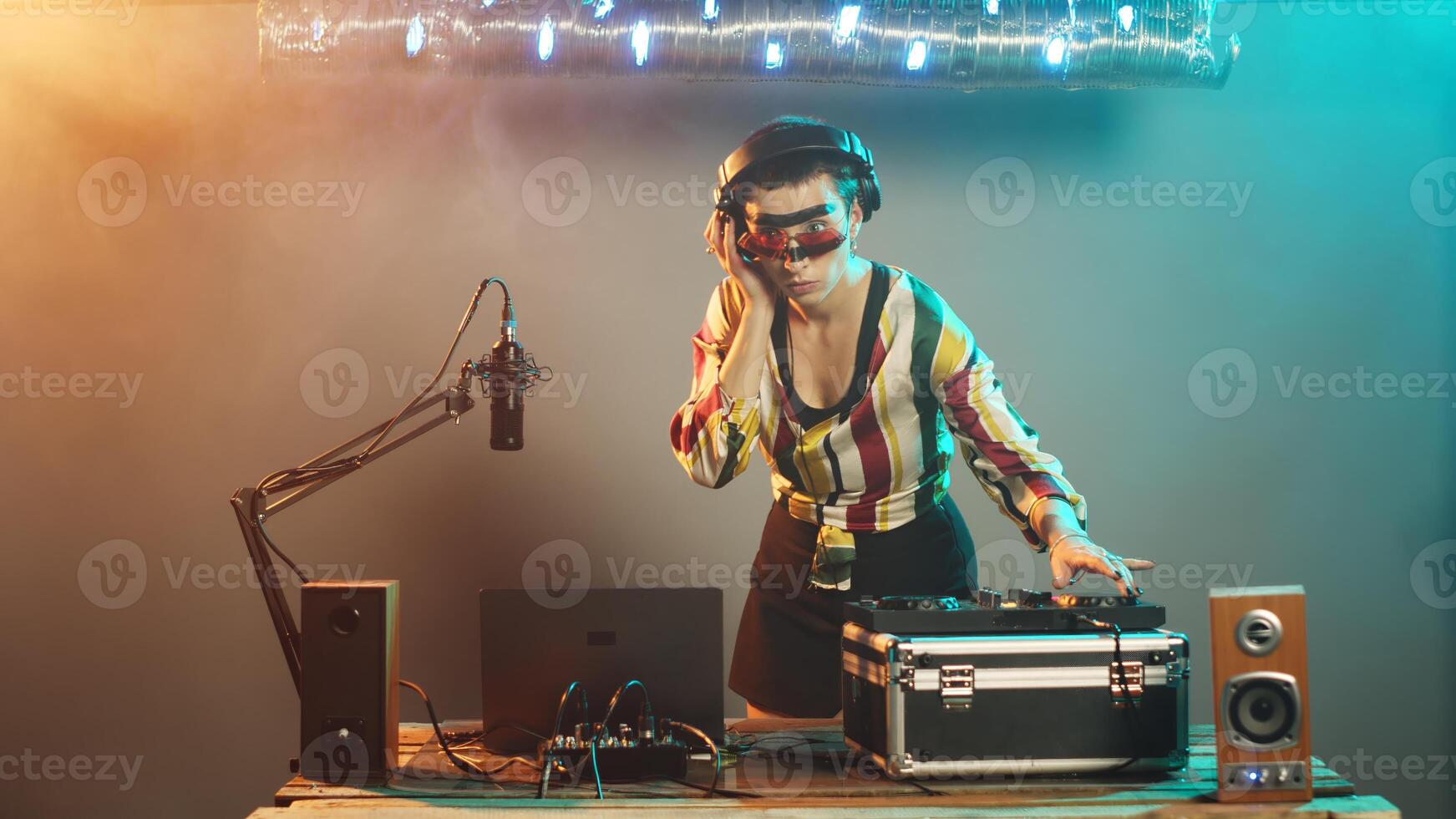 Musical artist using turntables to mix disco songs, producing sounds at dj stereo mixer with volume bass keys. Woman disc jockey working on remix performance show. Tripod shot. photo