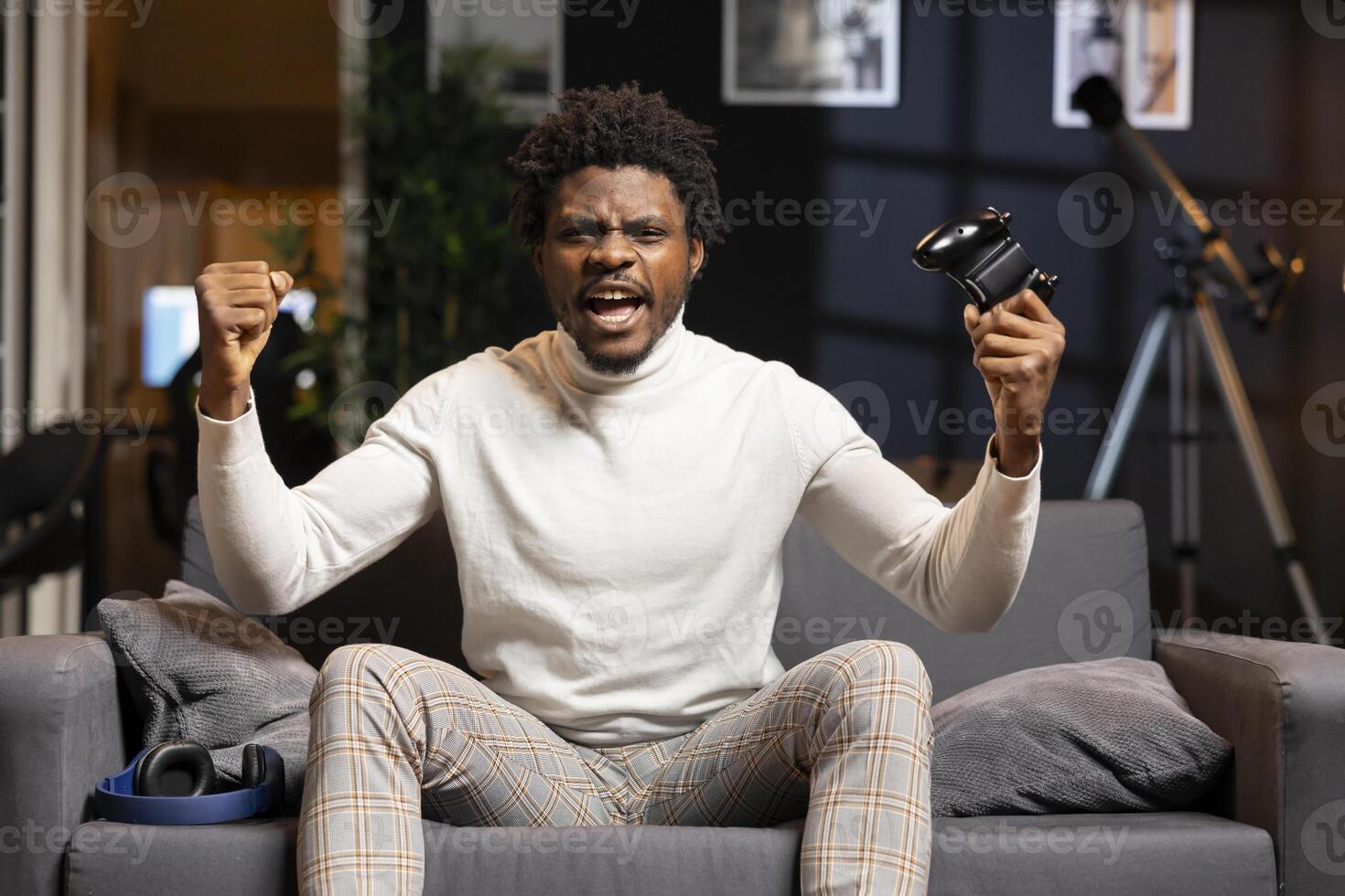 Happy BIPOC gamer celebrating after winning gaming console game in living room. Euphoric man bragging after being victorious in videogame, defeating all enemies using gamepad photo