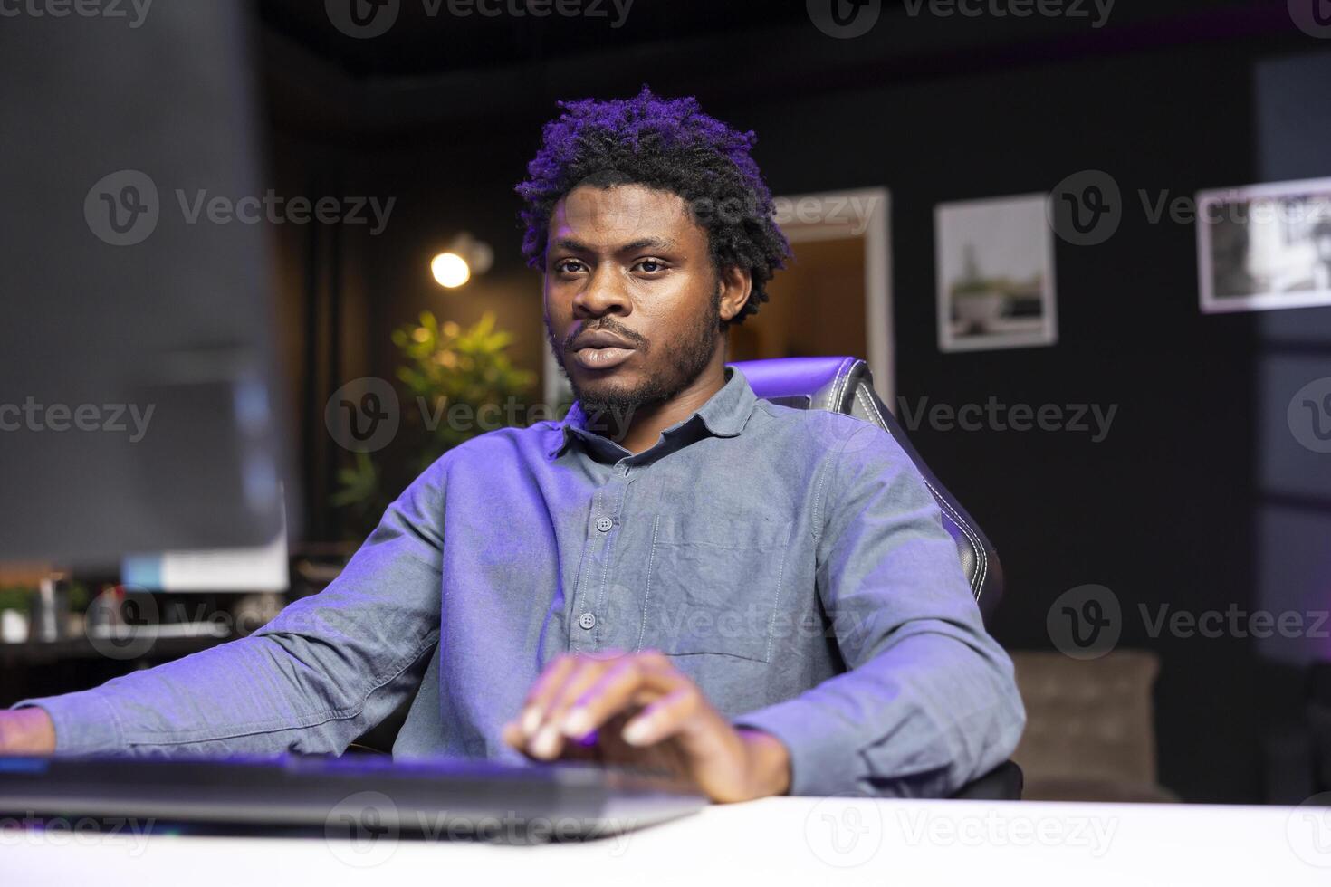 BIPOC man in living room playing engaging video games on gaming PC at computer desk, chilling after work. Gamer contending against foes in online multiplayer shooter using keyboard photo