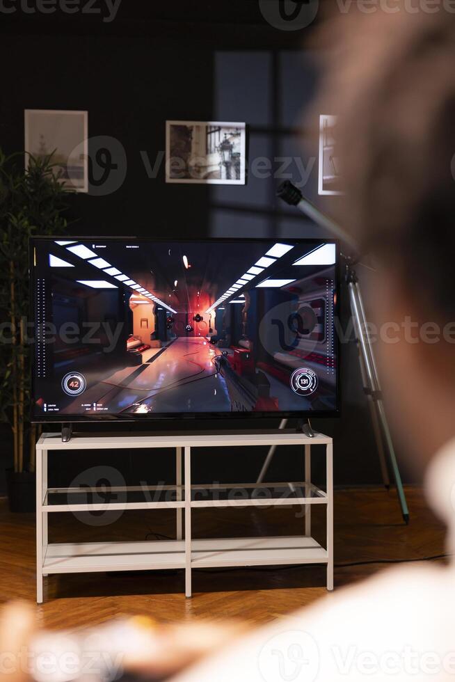 BIPOC man playing action videogames on smart TV, relaxing after long day at work. Gamer enjoying SF first person shooter game on gaming console, shooting laser bullets at enemies photo