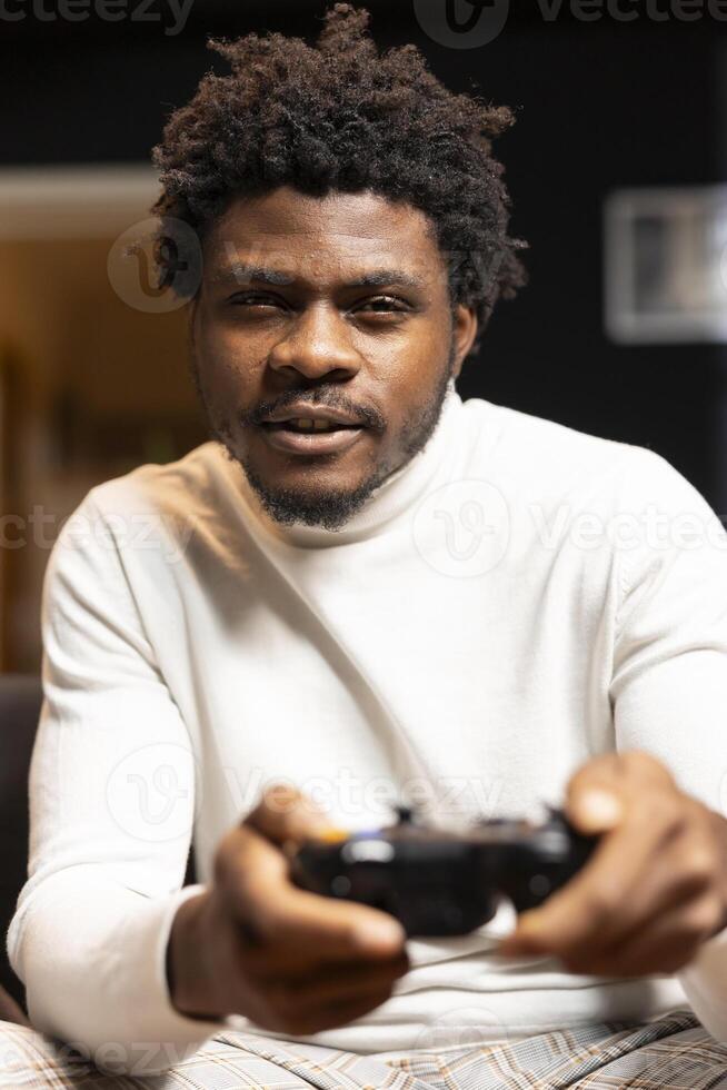 Portrait of cheerful BIPOC gamer engaging in online competitive multiplayer tourney using gaming console and gamepad. Player engaging in fun videogames, enjoying leisure time while defeating enemies photo