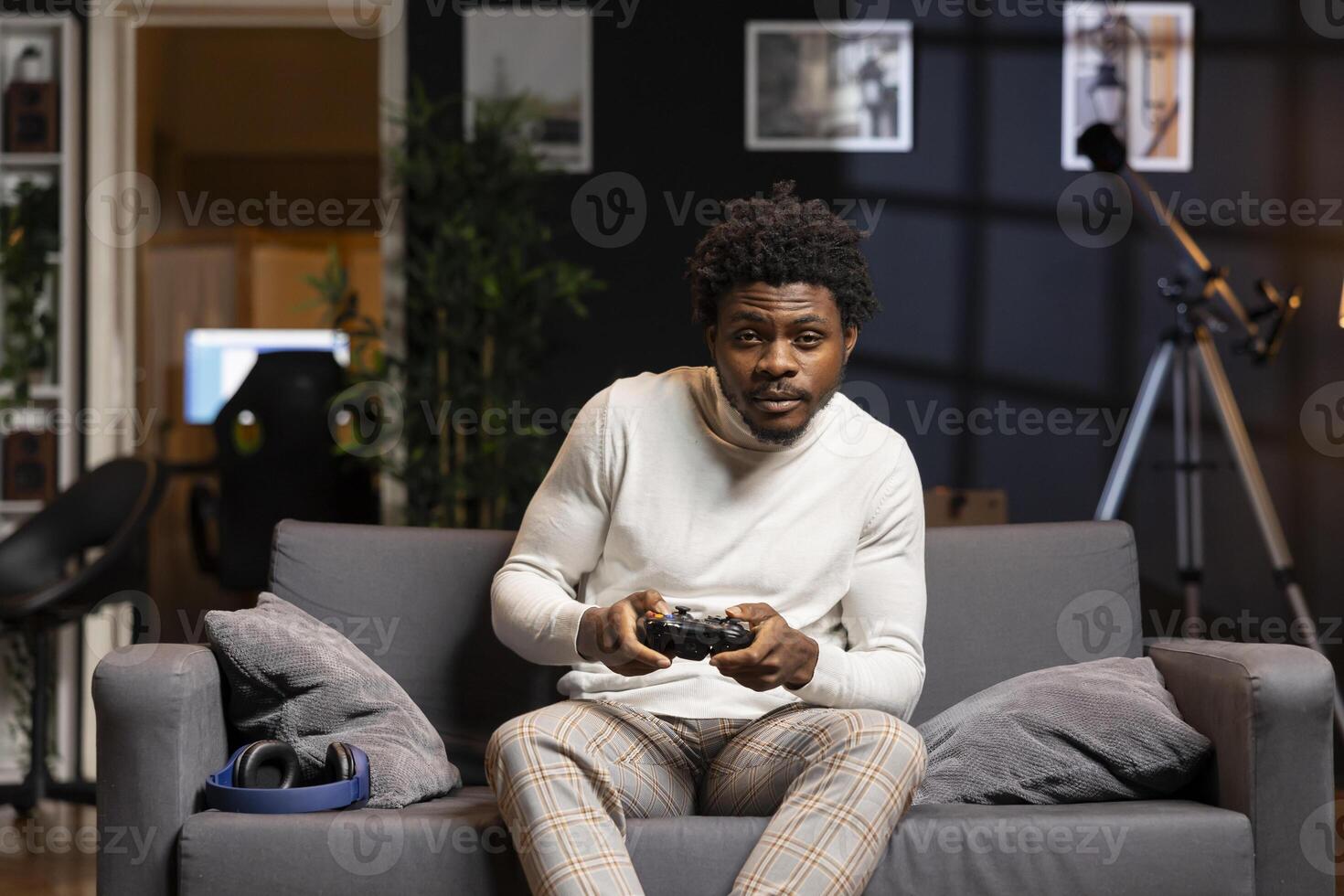 African american man playing videogame in home theatre, holding controller. Gamer participating in PvP online multiplayer game using console system and high quality gamepad photo