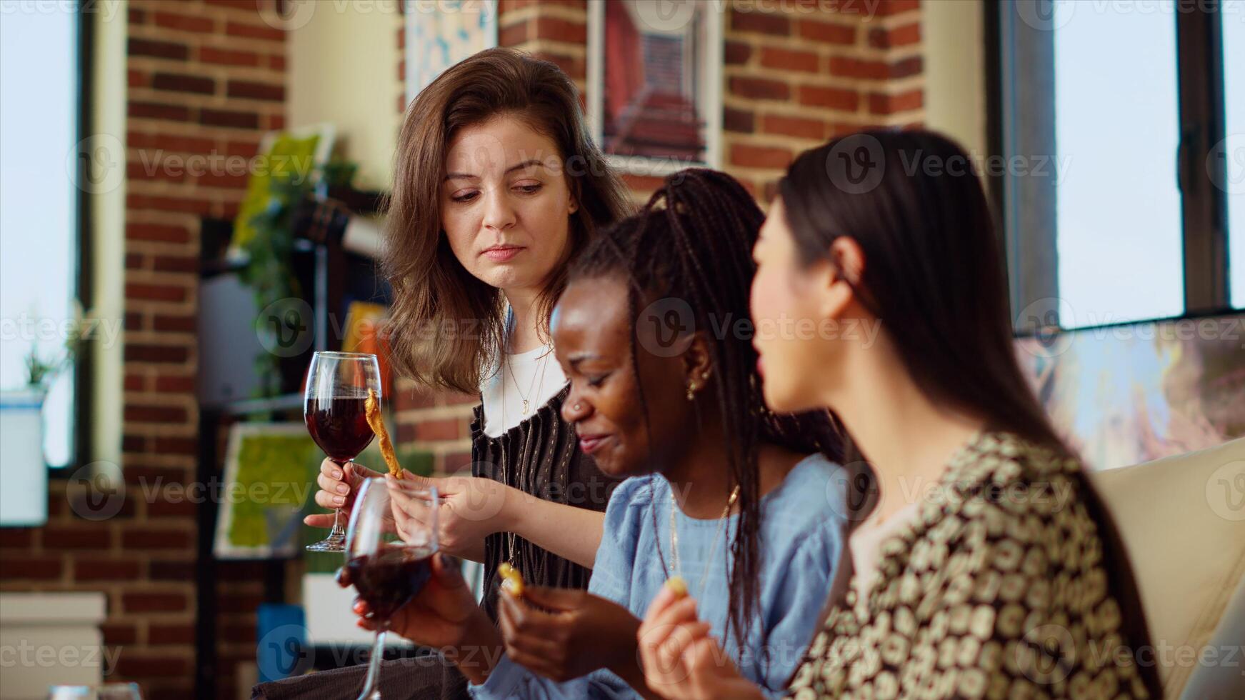 Close up on friends laughing, drinking alcohol beverages and eating crackers in cozy apartment living room. Colleagues spending time with each other, having lively conversation at home photo