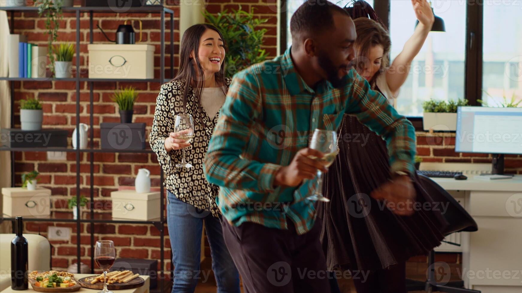 Multiracial group of friends dancing at apartment party, celebrating their friendship during annual reunion. Multiethnic colleagues doing energetic dance moves and laughing in cozy living room photo