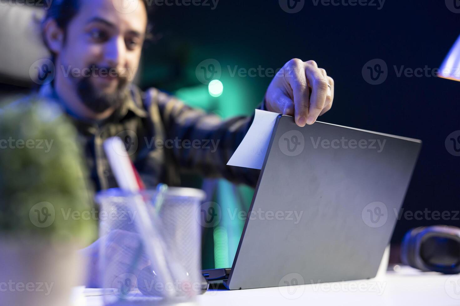 Close-up of a happy freelancer working from home, placing a sticky note on the screen of his laptop. A young man reviewing his research and study notes written on paper. photo