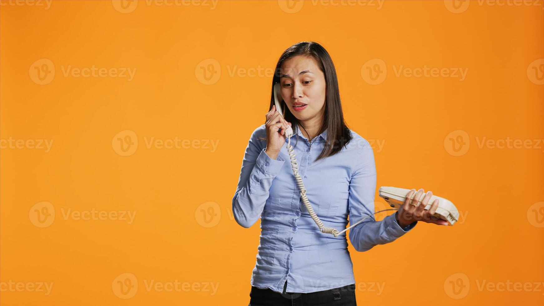 Asian person making remote call on landline phone as she speaks to somebody on old fashioned line. Confident woman handling office telephone with cable, interacting in studio remotely. photo