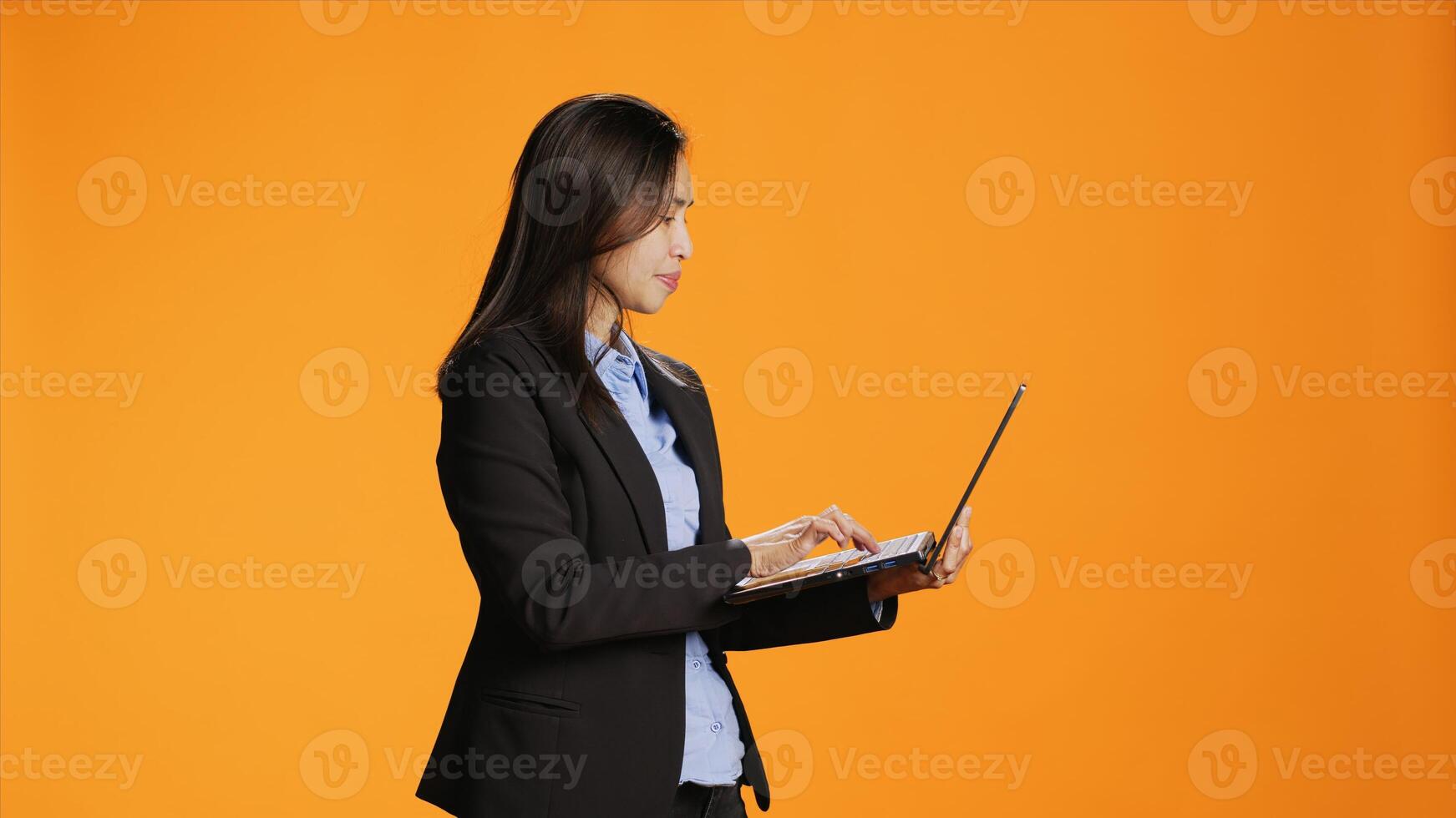 Businesswoman browsing sites on laptop in studio, looking for inspiration or research on portable computer against orange background. Asian girl checking webpages on internet, search engine. photo