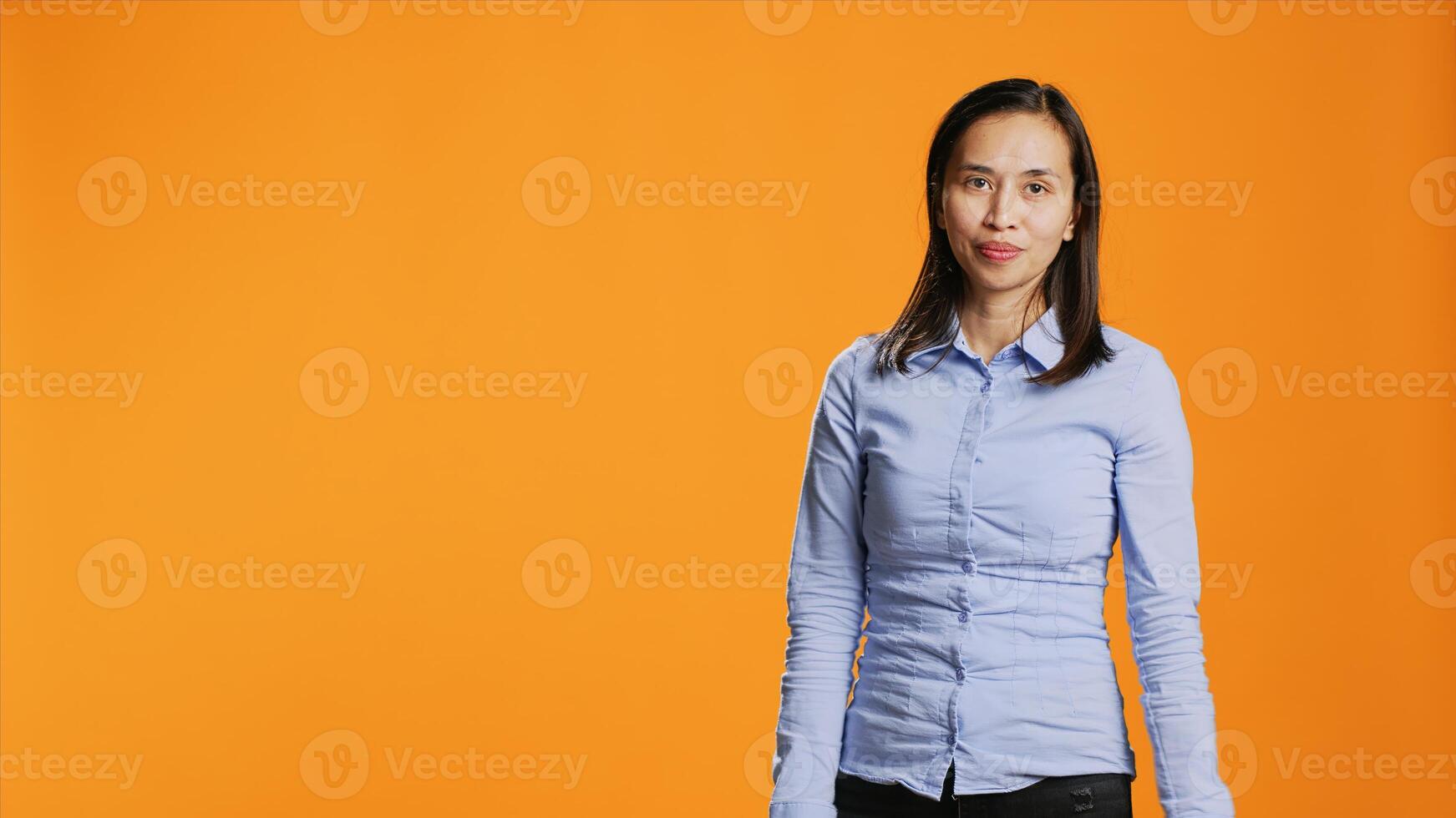 Asian person presenting something to studio sides, creating new marketing advertisement posing over orange background. Young woman pointing left or right for web promotional ad. photo