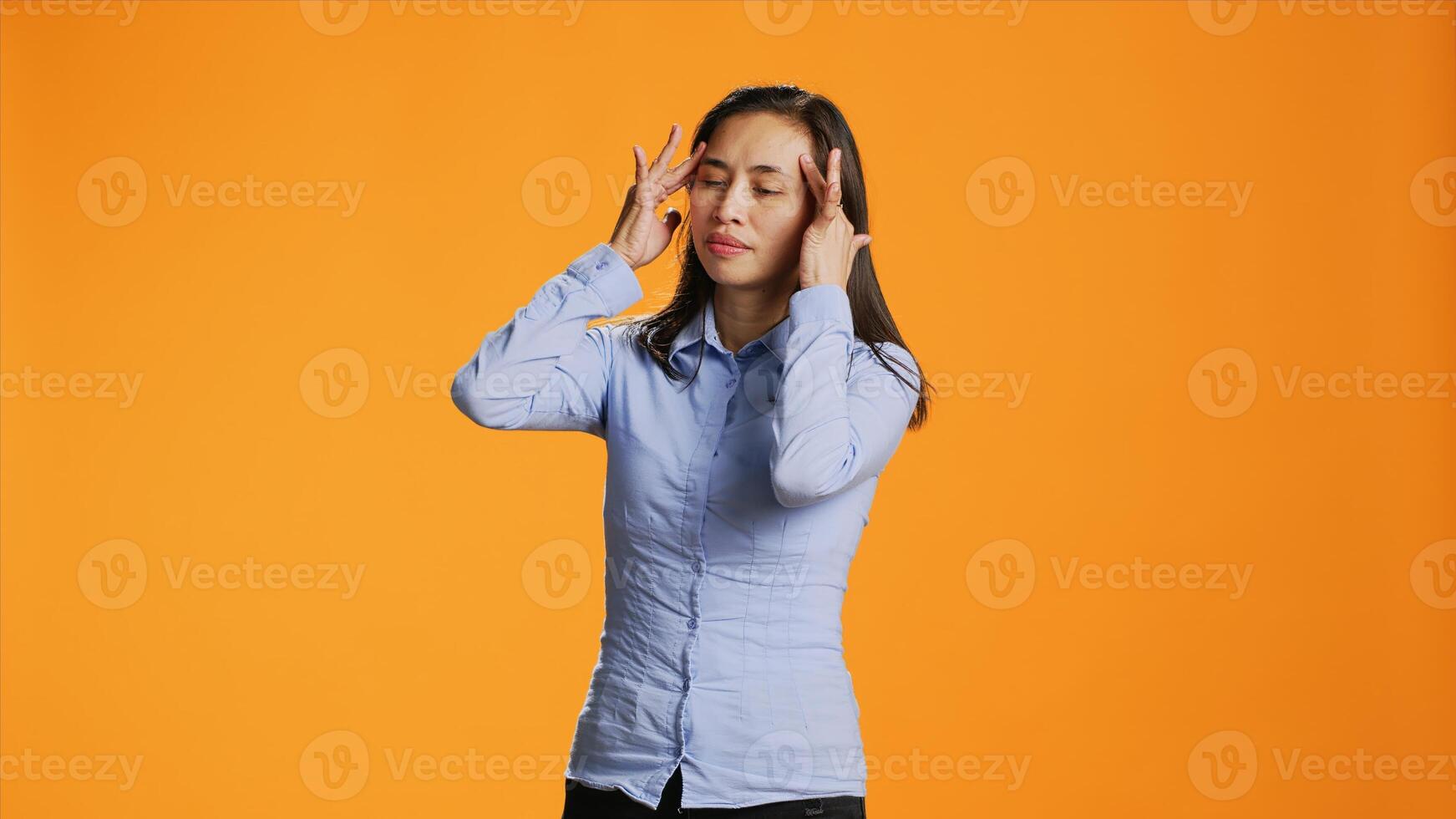 Asian young adult suffers from painful migraine in studio, rubbing temples to ease temples pressure. Sick worried woman feeling under stress, dealing with headache and tension. photo