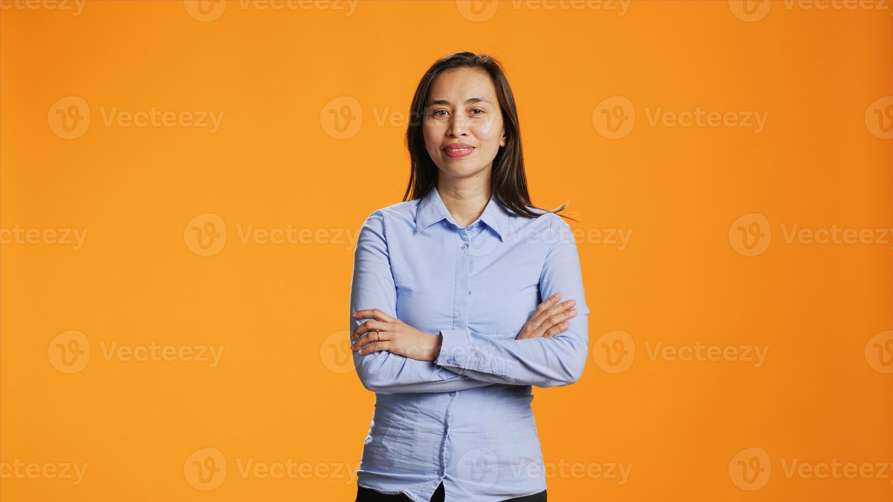 retrato de alegre persona en pie en brazos cruzado posando terminado naranja fondo, sonriente a cámara durante glamour disparo. positivo filipino mujer con satisfecho expresión disfrutando felicidad. foto