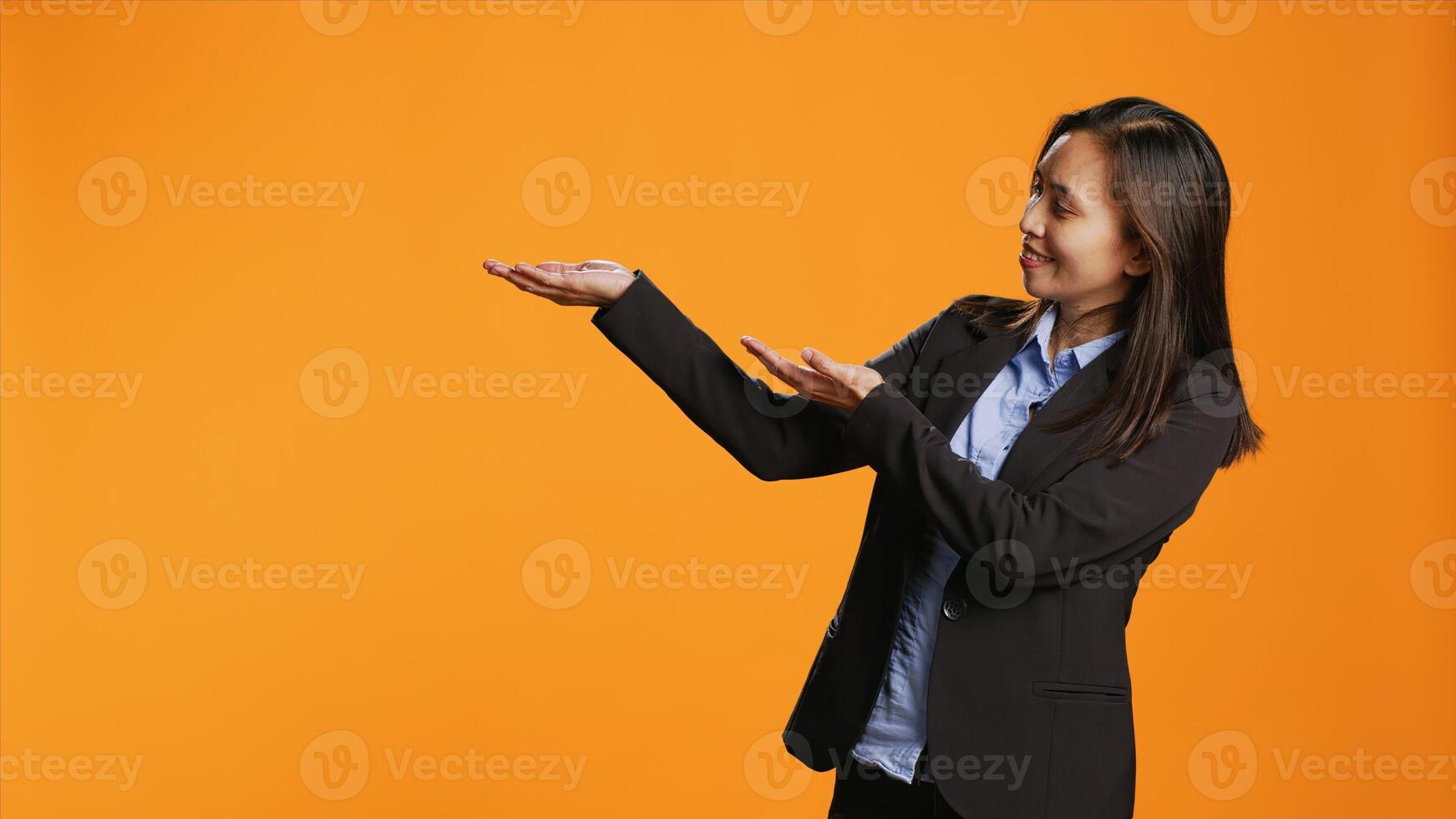 Businesswoman shows left and right directions in studio, creating new internet advertisement over orange background. Asian person working on marketing web commercial on camera. photo