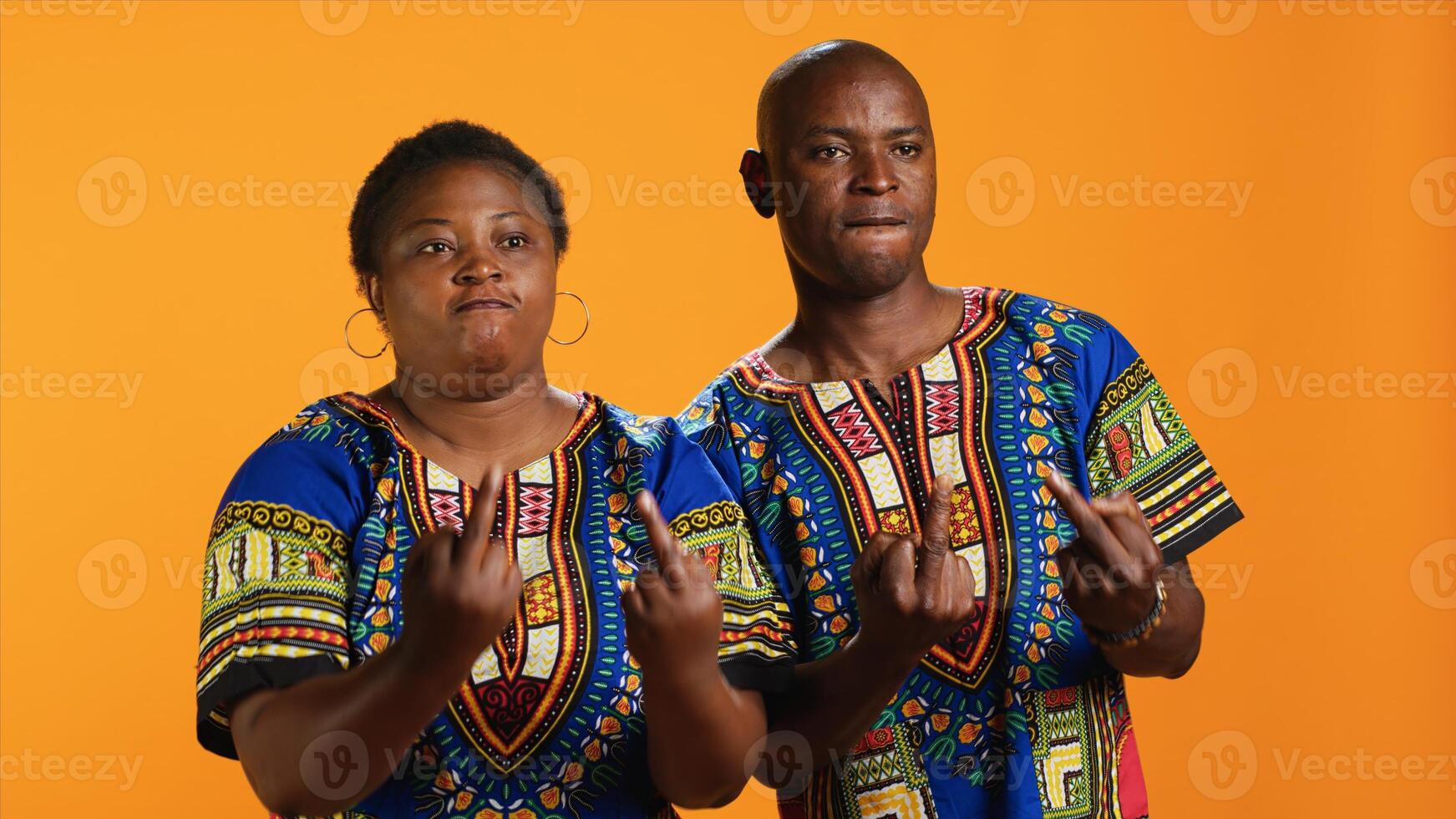 Rude ethnic couple showing middle finger in studio, doing offensive provocative gesture over orange background. Furious violent man and woman starting fight, negative hooligan symbol. photo