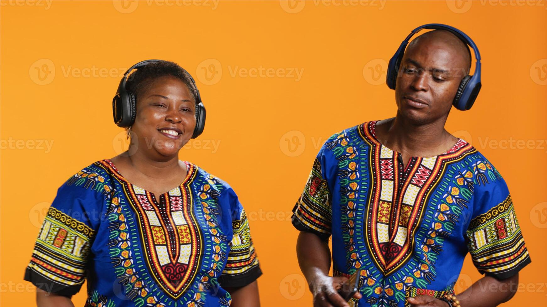 Joyful young couple enjoying music on headphones, dancing on camera on their wedding song and having fun. Ethnic married people feeling happy showing cool dance moves in studio. photo