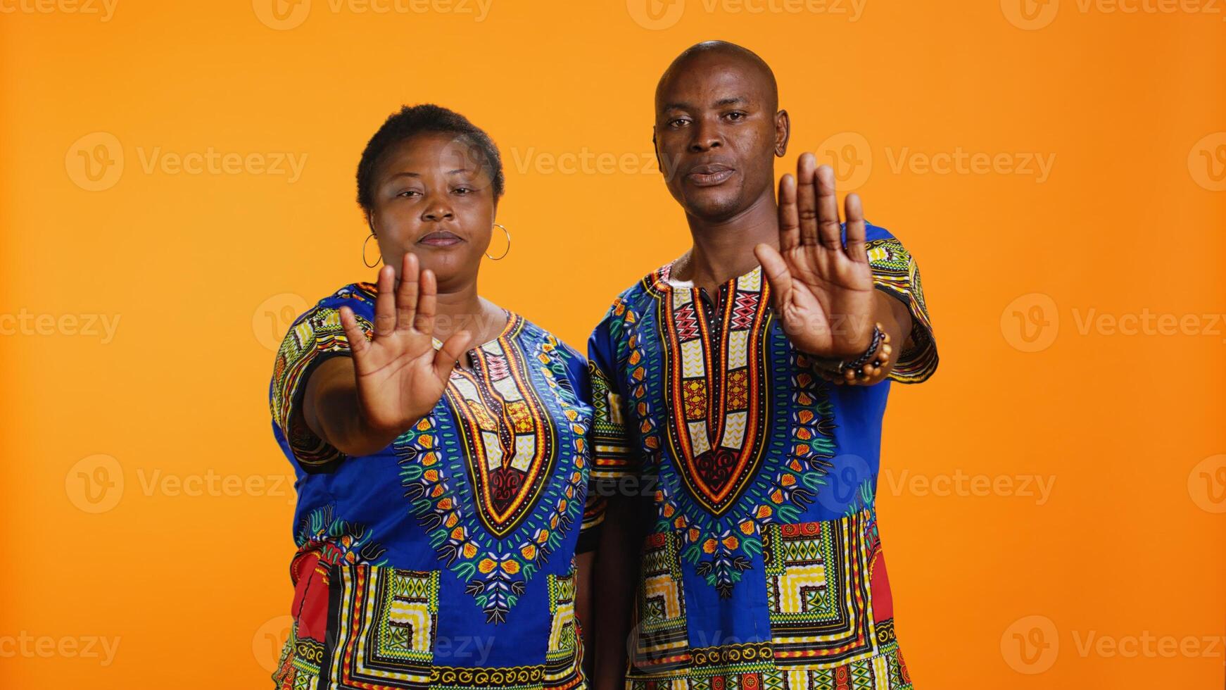 Confident ethnic couple showing stop sign in studio, raising palm and expressing their rejection. Man and woman doing refusal negative symbol, being displeased and disappointed. photo