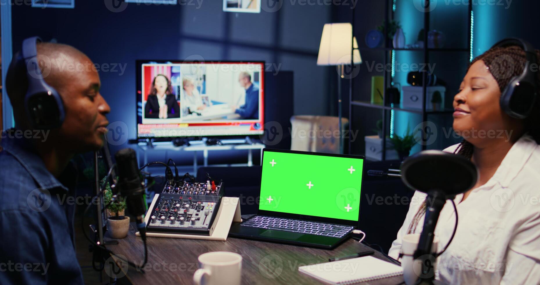 Green screen laptop next to vlogger show host and guest talking in neon lights ornate living room personal studio. Mockup notebook next to man and woman broadcasting discussion on online podcast photo