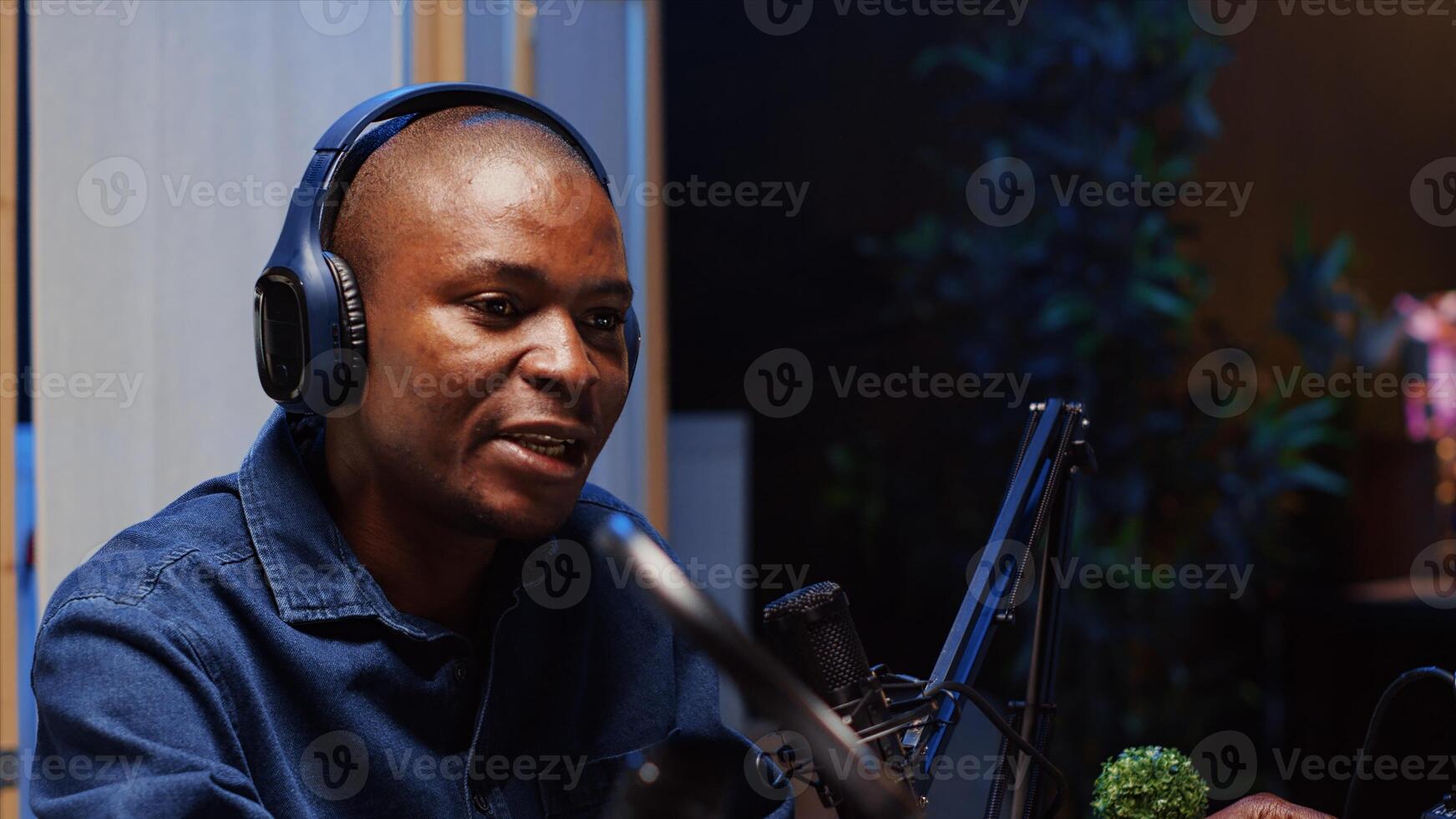 African american man doing podcast in studio, wearing headphones and talking on professional microphone with guest. Close up shot of BIPOC content creator interviewing another person photo