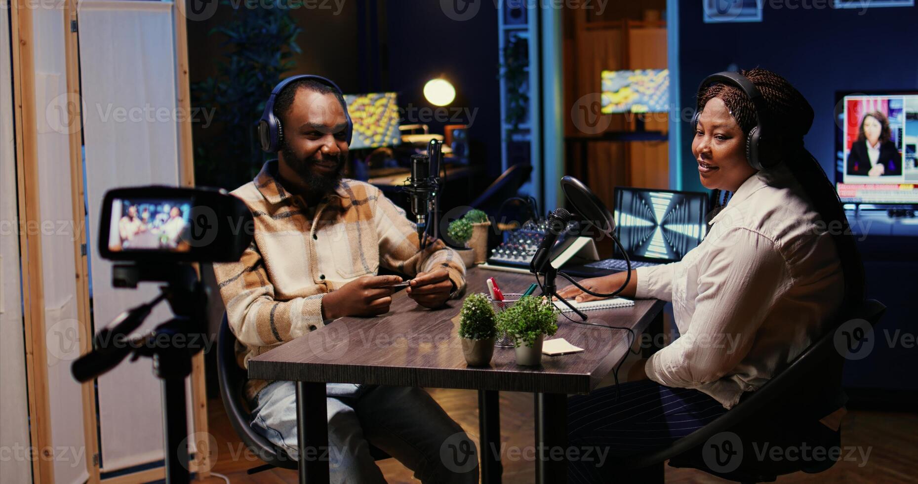 Man and woman laughing during comedy focused podcast filmed with professional camera. African american guest amused by talking show host telling jokes, recording with high tech equipment photo