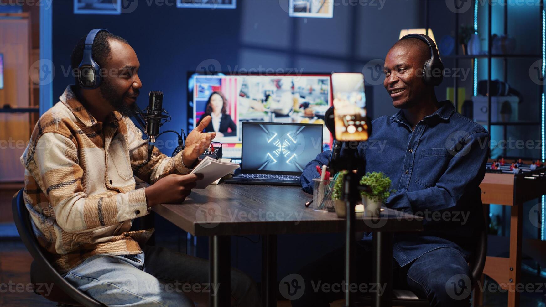 Content creator recording interview with smartphone on tripod in studio, reviewing notes to ask quality questions to guest. Journalist using mobile phone to film vlog, talking on mic with man photo
