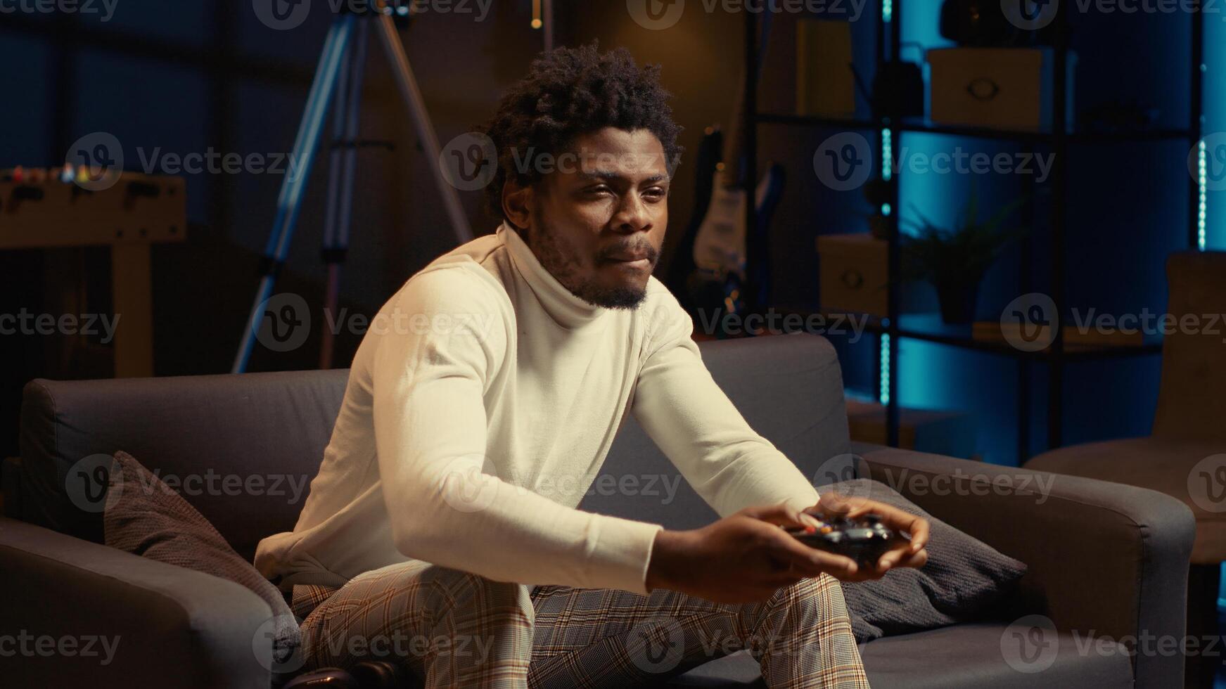 Energetic african american man playing videogames on couch, using spamming buttons on motion controlled controller. Player battling opponents in internet multiplayer game on console photo