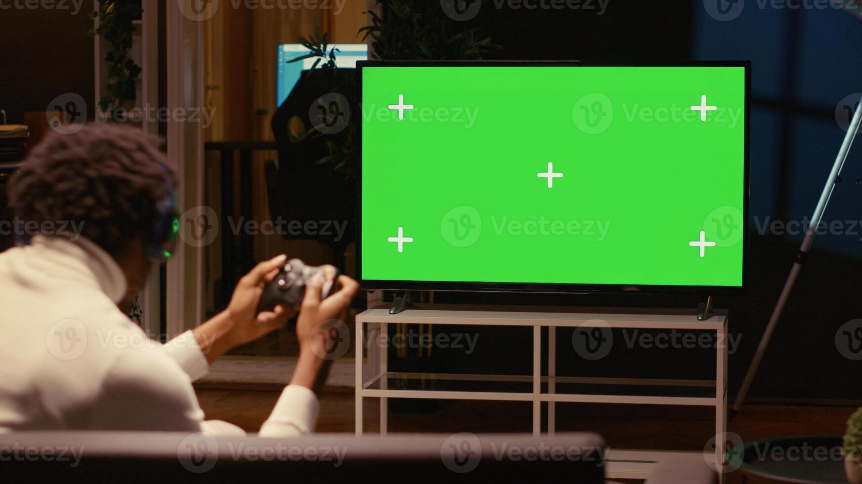 Man in dimly lit apartment playing video games on green screen widescreen smart TV, enjoying day off from work. Gamer battling enemies in online multiplayer shooter on gaming console photo