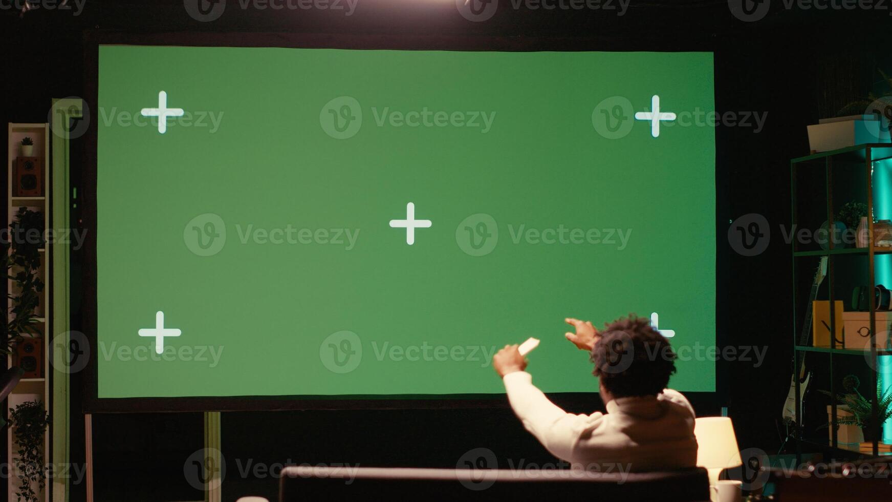 African american man watching football competition live on widescreen chroma key smart TV, cheering for favorite team. Sports fan on couch in front of green screen television set celebrating goal photo